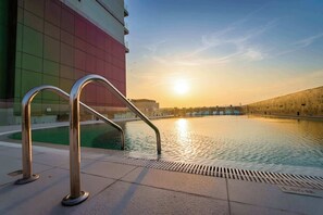 Une piscine avec des garde-corps en métal, un ciel dégagé et un bâtiment en arrière-plan.