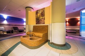 Ein Wellnessbereich mit einer großen, runden, gewebten Badewanne, einer Holzbank und einem an der Wand hängenden Bild eines Waldes.