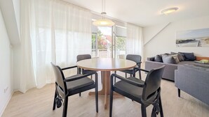 Uma sala de estar moderna com uma mesa redonda e quatro cadeiras, um sofá cinzento e um quadro na parede.
