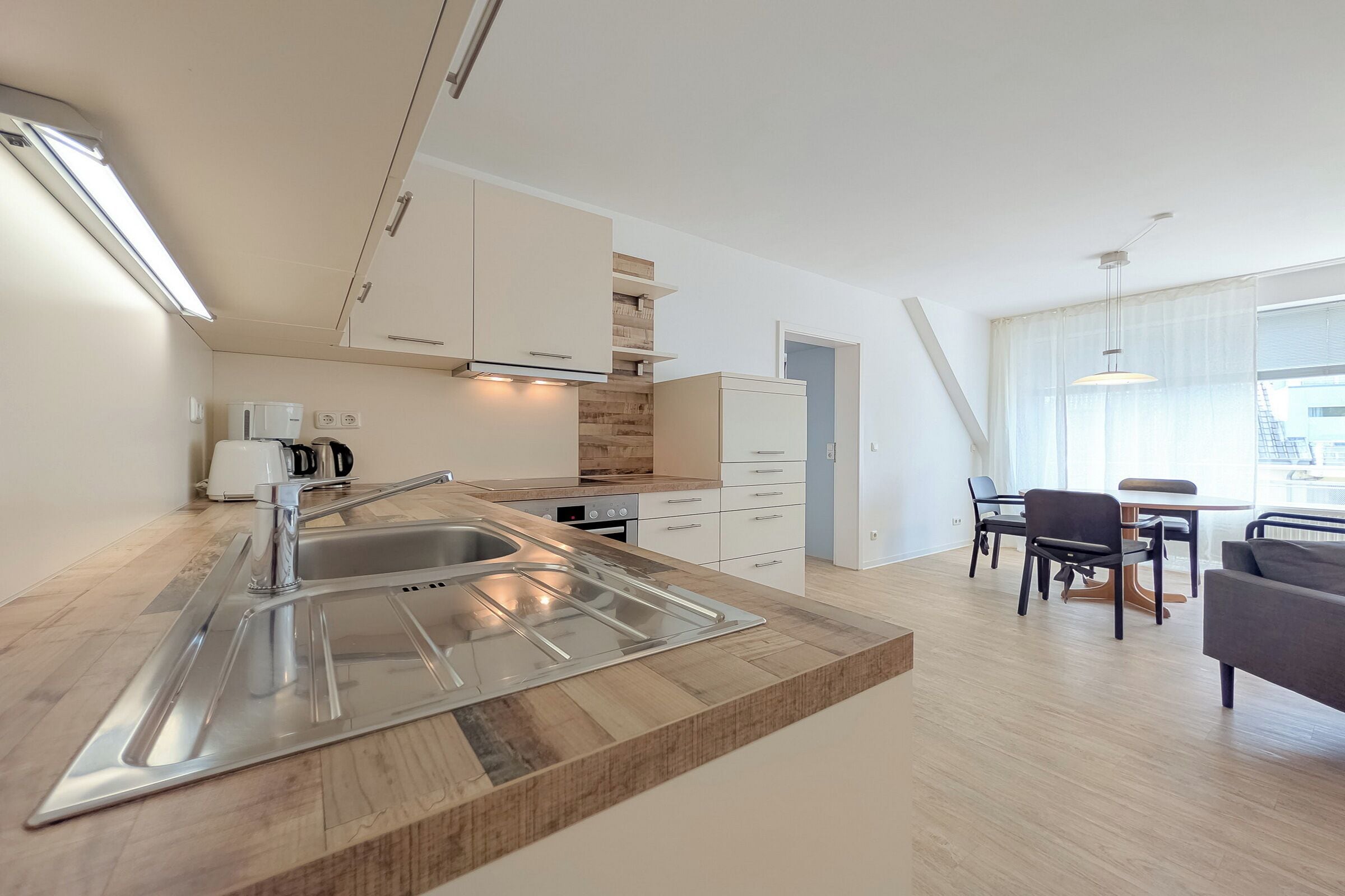 Eine moderne Küche mit Spüle aus Edelstahl, einer Holz Arbeitsplatte und weißen Schränken.