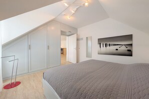 Une chambre avec un grand lit, un tableau accroché au mur et un escalier menant à une autre pièce.