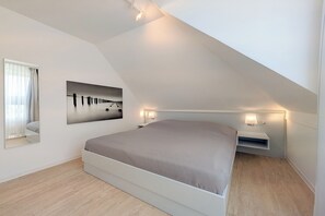 A modern bedroom with a sloped ceiling, a large bed, a bedside table with a lamp, and a wall-mounted picture. - Seestern Residence, Apartment 32 (Ostseebad Boltenhagen)