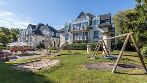 Um edifício residencial com parquinho, incluindo escorrega e baloiços, e área de pátio com mobiliário de exterior.