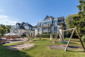 Ein Wohngebäude mit Spielplatz, inklusive Rutsche und Schaukeln, sowie einer Terrassenfläche mit Sitzgelegenheiten.