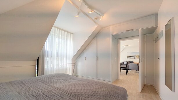 Quarto com cama grande, claraboia e vista para um outro espaço.