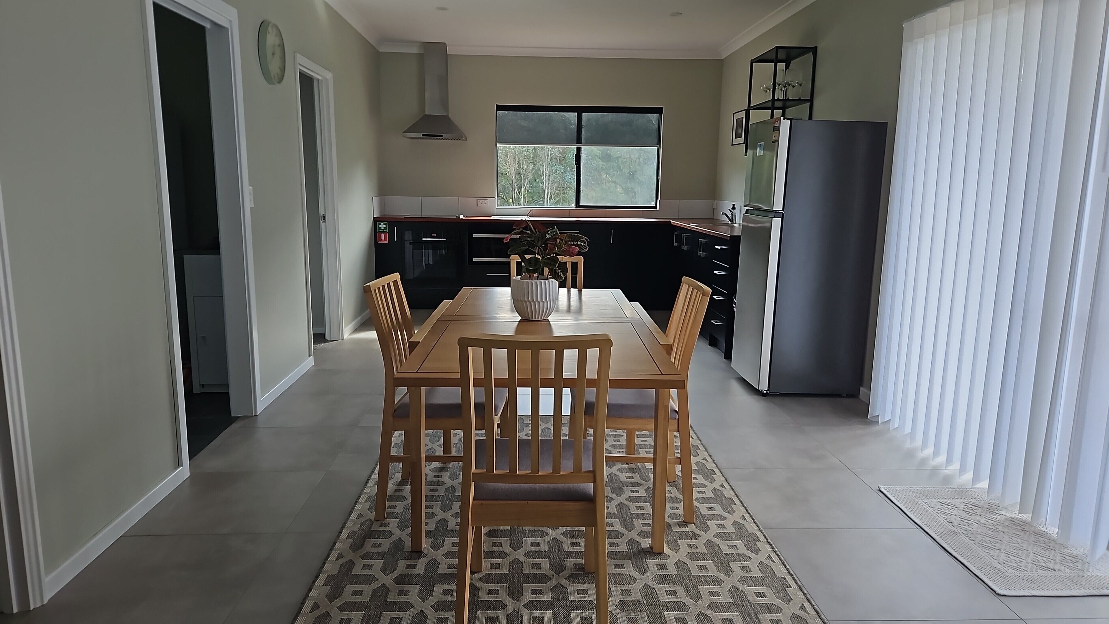 A modern kitchen with a dining area, featuring a large window, a built-in oven, and a refrigerator.