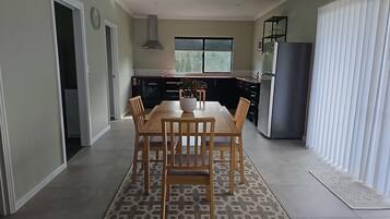 A modern kitchen with a dining area, featuring a large window, a built-in oven, and a refrigerator.