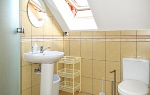 A bathroom with a skylight, a sink, a toilet, and a small shelf with baskets.