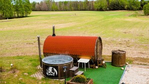 A hot tub with a wooden barrel exterior, a small table, and a wooden stool in a grassy field with trees in the background. - Nice apartment in Przechlewo with sauna (Przechlewo)