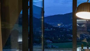 A room with a glass door leading to a view of a town at dusk. - Amazing apartment in Miedzybrodzie Zywiec (Miedzybrodzie Zywiec)