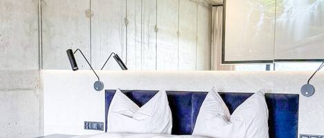 Une chambre moderne avec un grand lit, une table de chevet, une lampe fixée au mur et un écran de projection diffusant une image de cascade.