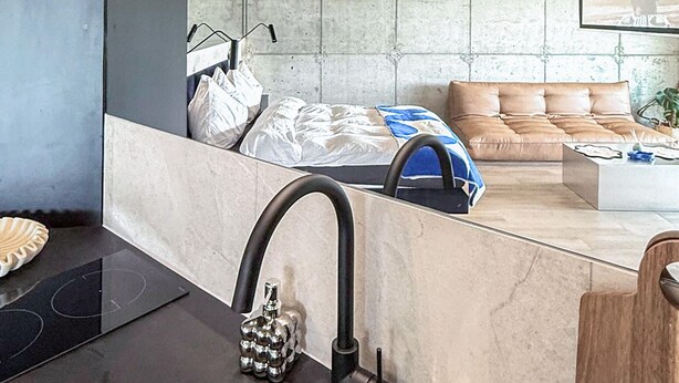 A modern bedroom with a bed, a sofa, a coffee table, and a bathroom with a sink and mirror. - Amazing apartment in Miedzybrodzie Zywiec (Miedzybrodzie Zywiec)