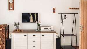 Ein Zimmer mit einem Holztisch, einem Flachbildfernseher, einem Radio und einer schwarzen Metallregaleinheit.