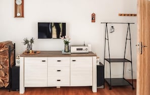 Ein Zimmer mit einem Holztisch, einem Flachbildfernseher, einem Radio und einer schwarzen Metallregaleinheit.