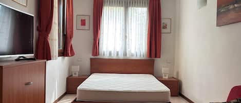 A bedroom with a bed, a TV, a red sofa, and a window with curtains.