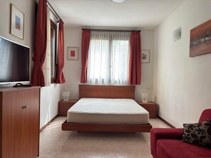 A bedroom with a bed, a TV, a red sofa, and a window with curtains. - Casa Leopardi - apartment in Garda (Garda)