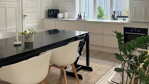 A modern kitchen with a large island, white cabinetry, and a view through the window. - Grand 1912 apartment in inner Østerbro (København)