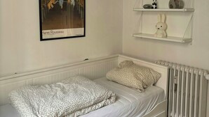 A bedroom with a single bed, a radiator, and a wall-mounted shelf with decorative items. - Grand 1912 apartment in inner Østerbro (København)