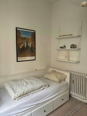 Ein Schlafzimmer mit einem Einzelbett, einem Heizkörper und einem an der Wand befestigten Regal mit Dekoration.