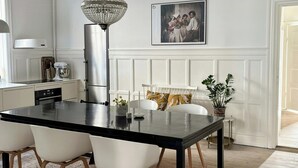 A dining area with a black table, white chairs, a chandelier, and a framed picture on the wall. - Grand 1912 apartment in inner Østerbro (København)