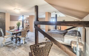 Ein geräumiges Schlafzimmer im Loft-Stil mit einem großen Bett, einem Holzbalken an der Decke und Blick auf den Wohnbereich.