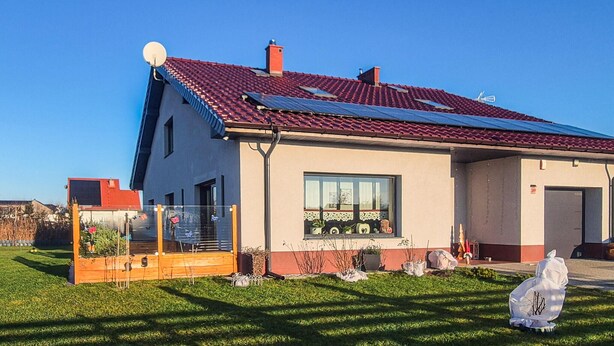Una casa moderna con techo de tejas rojas, paneles solares y un césped cuidado.