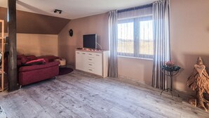 Una habitación con un sofá rojo, un armario blanco, un televisor de pantalla plana, una ventana con cortinas y una pequeña mesa con un jarrón.