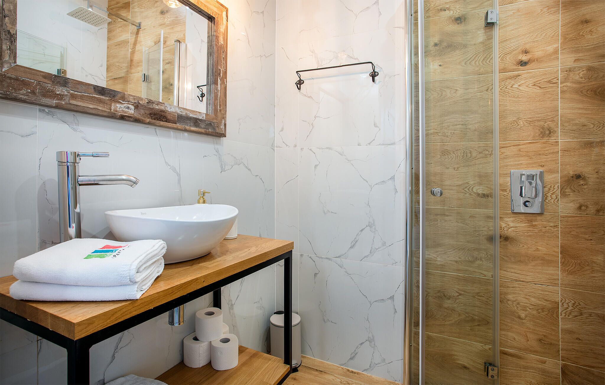 A bathroom with a white sink, a wooden vanity, a mirror, and a glass shower enclosure.
