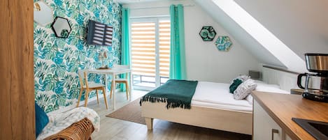 A bedroom with a bed, a desk, a chair, a television, and a coffee maker.