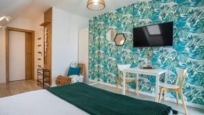 A room with a bed, a desk, chairs, a television, and a wall with a leafy pattern. - Gorgeous apartment in Nowecin with WiFi (Nowecin)