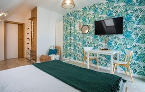 A room with a bed, a desk, chairs, a television, and a wall with a leafy pattern. - Gorgeous apartment in Nowecin with WiFi (Nowecin)