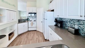 Una cocina con armarios blancos, estufa, refrigerador y cafetera.