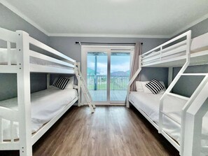 Une chambre avec deux lits superposés, une porte-fenêtre coulissante donnant sur un balcon et un plancher en bois.
