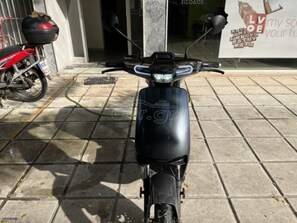 Ein schwarzer Roller auf einem gefliesten Bürgersteig.