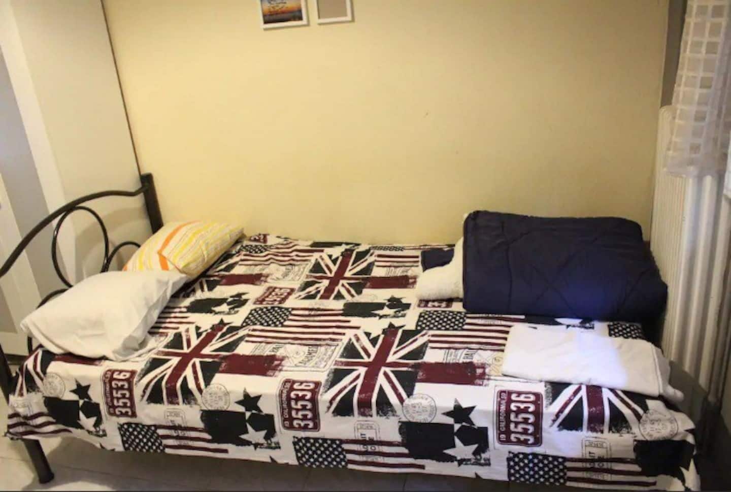 Un lit simple avec une courtepointe ornée de plusieurs drapeaux, un oreiller blanc et un oreiller foncé.