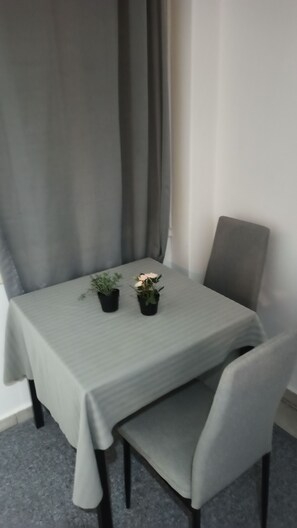 Ein Esstisch mit einer hellgrünen Tischdecke, zwei Blumentöpfen und einem grau gepolsterten Stuhl.