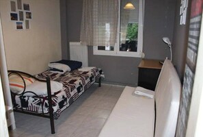 Ein kleines Zimmer mit einem Einzelbett, einem Fenster, einem Heizkörper und einem Schreibtisch.