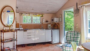 Een kleine keuken met witte kastjes, een magnetron en een spoelbak. Er is een raam met uitzicht op groen.