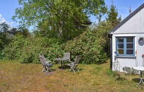 A rustic outdoor seating area with wooden chairs and a table, surrounded by lush greenery and a wooden building with a window. - Stunning home in Borrby (Borrby)
