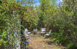An outdoor seating area with metal chairs and a table, surrounded by dense foliage and trees. - Stunning home in Borrby (Borrby)