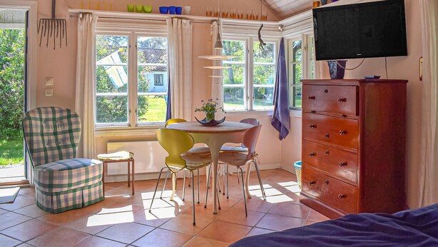 Een kamer met een eettafel, stoelen, een televisie, een kast en een raam met gordijnen.