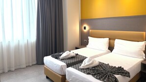 A hotel room with two beds, a large window with curtains, a wall-mounted light, and a plain wall with a yellow accent. - Hotel Lume (Milano)