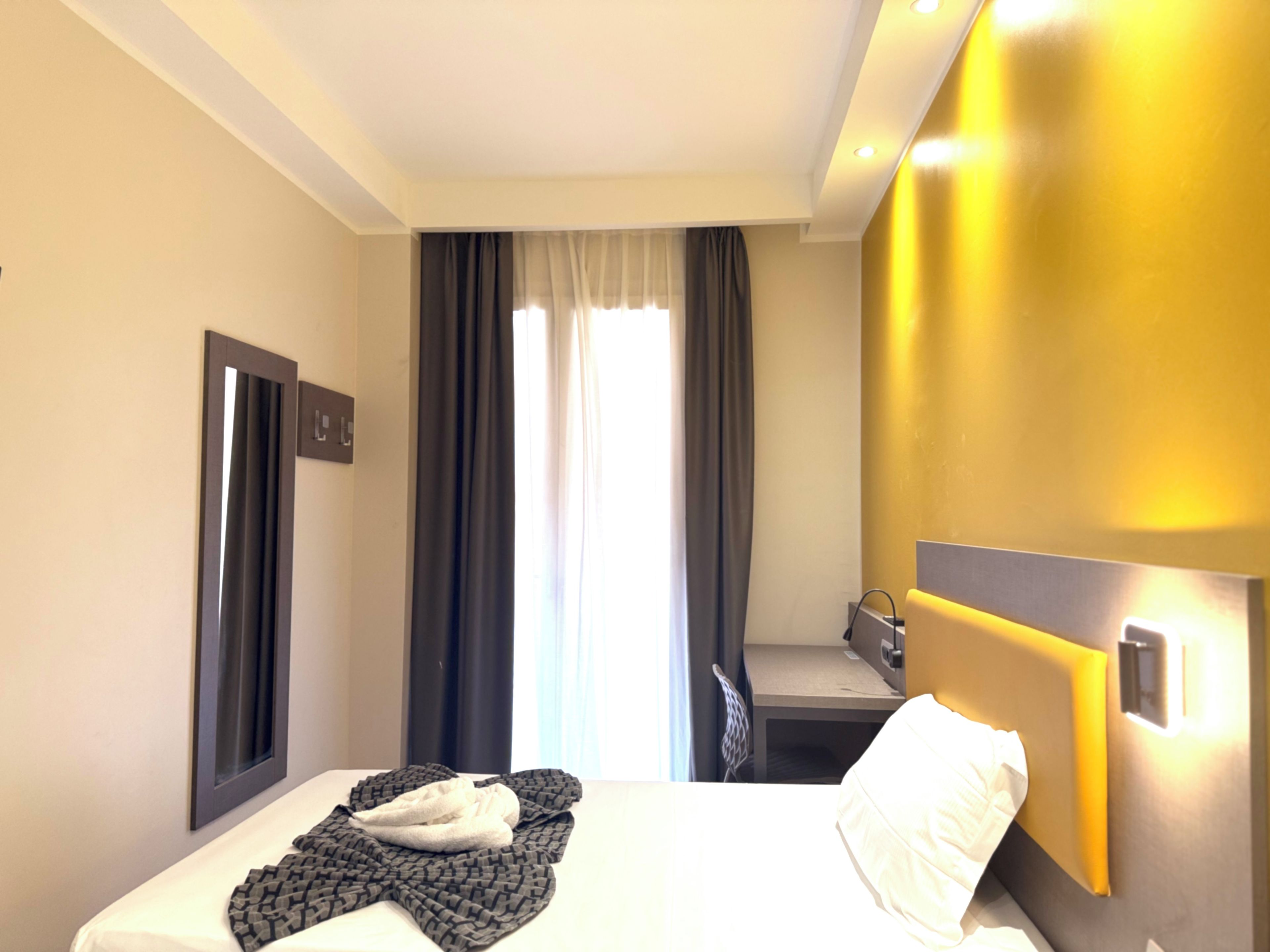 A hotel room with a bed, a desk, and a window with curtains.