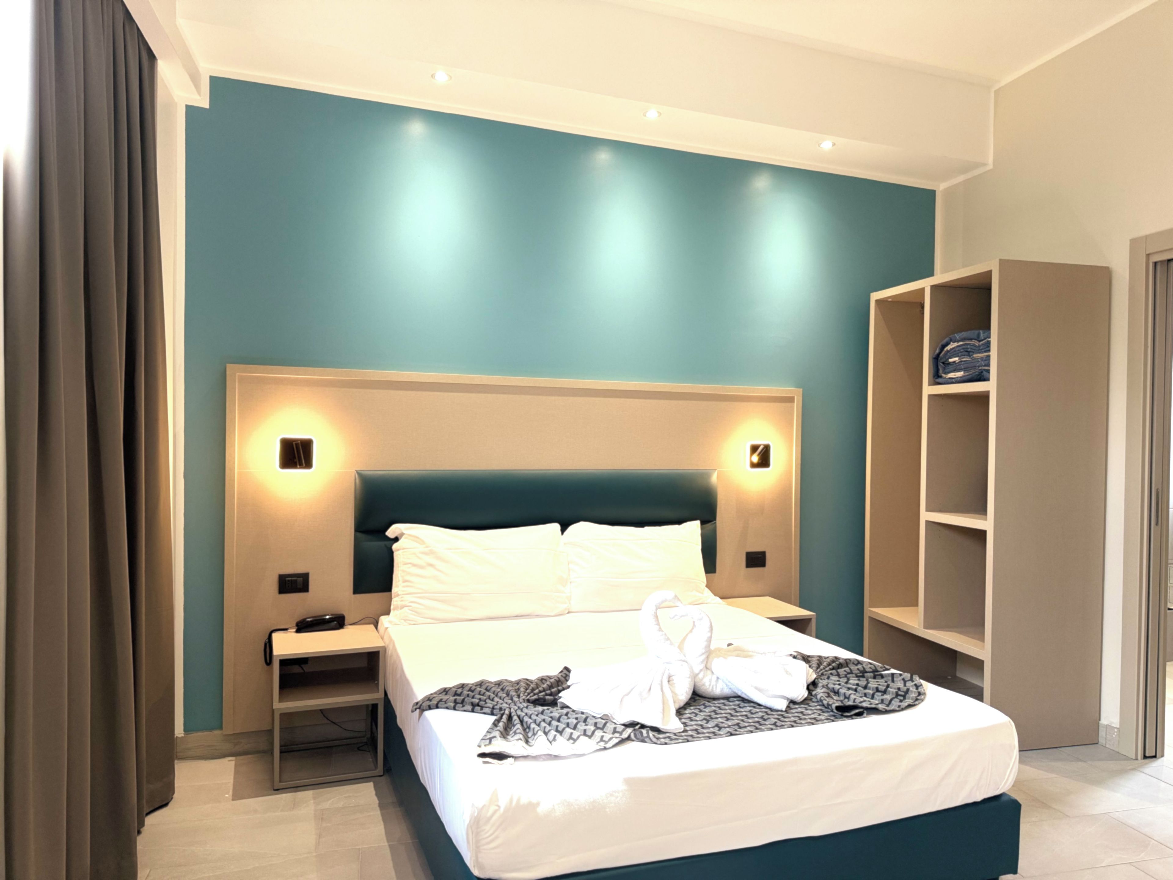 A hotel room with a bed, bedside tables, a wardrobe, and a wall-mounted light fixture.