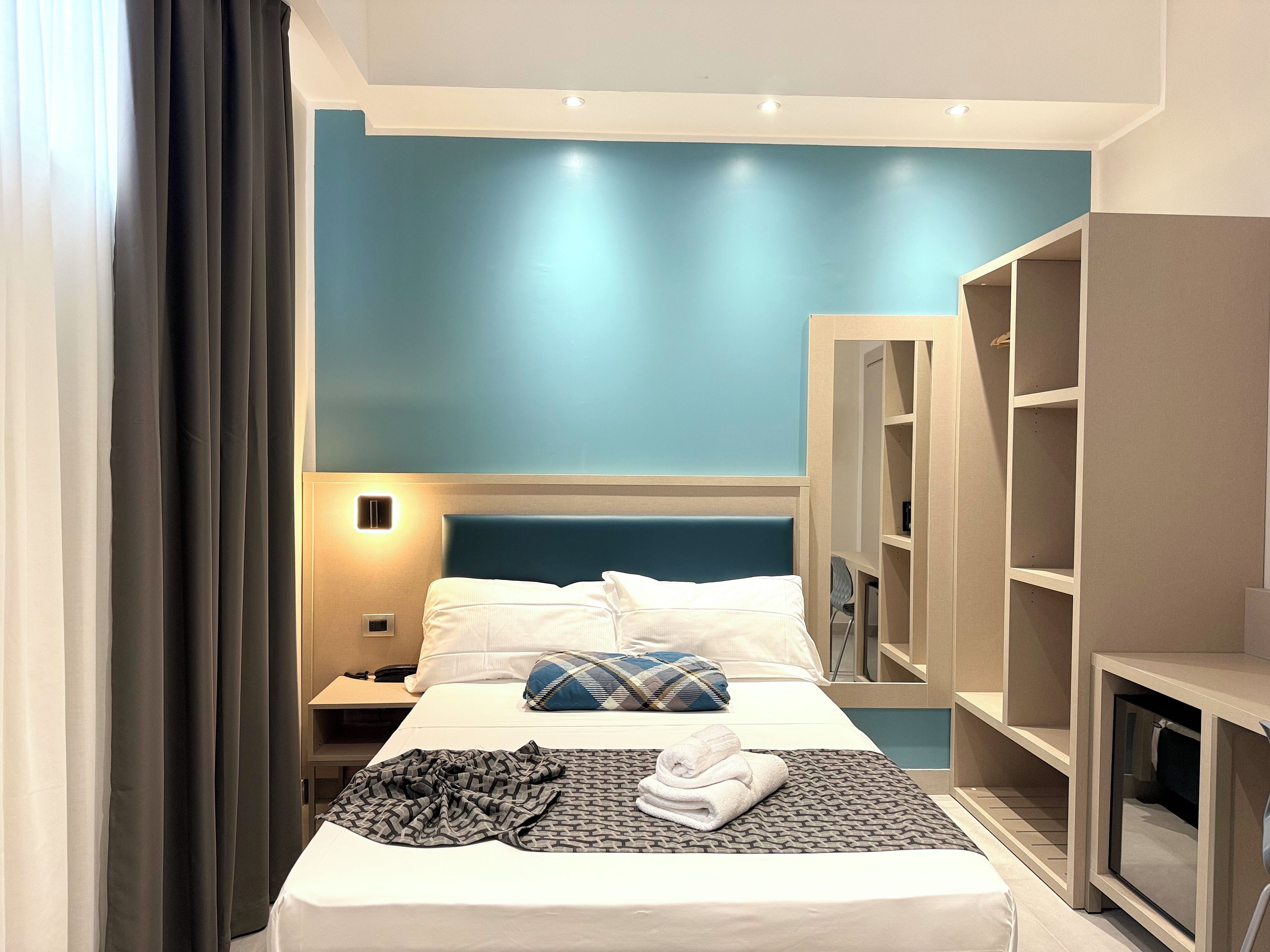 A hotel room with a bed, a bedside table, a lamp, a wardrobe, and a mirror.
