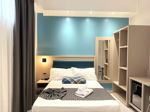 Hotellihuone, jossa on sänky, yöpöytä, lamppu, vaatekaappi ja peili.