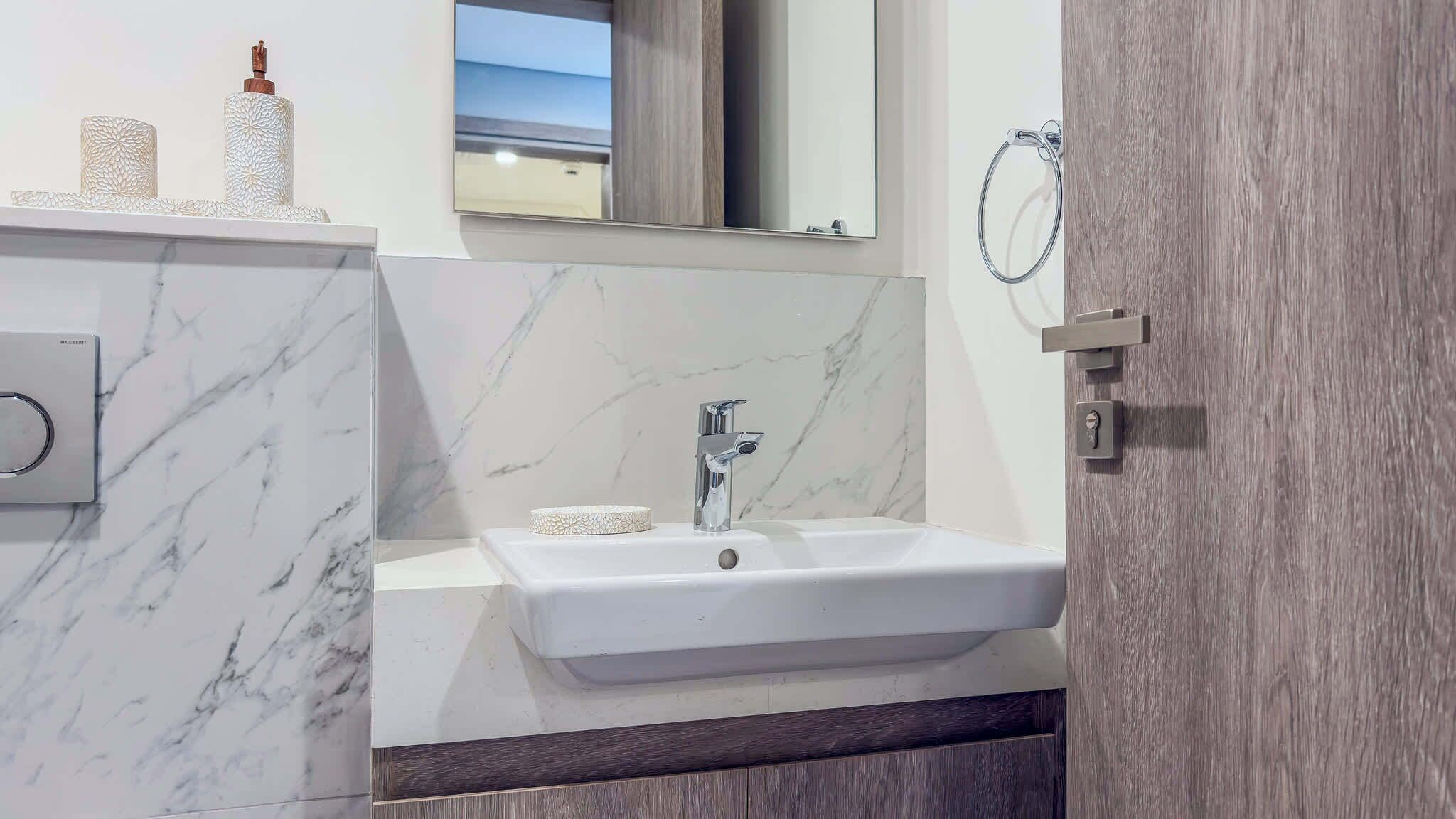 A bathroom with a marble wall, a sink, a mirror, and a towel ring.