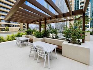 An outdoor patio with a table and chairs, surrounded by greenery and overlooking a cityscape. - Luxury 2BR Plus Maids, High-Floor Marina Views (Dubai)