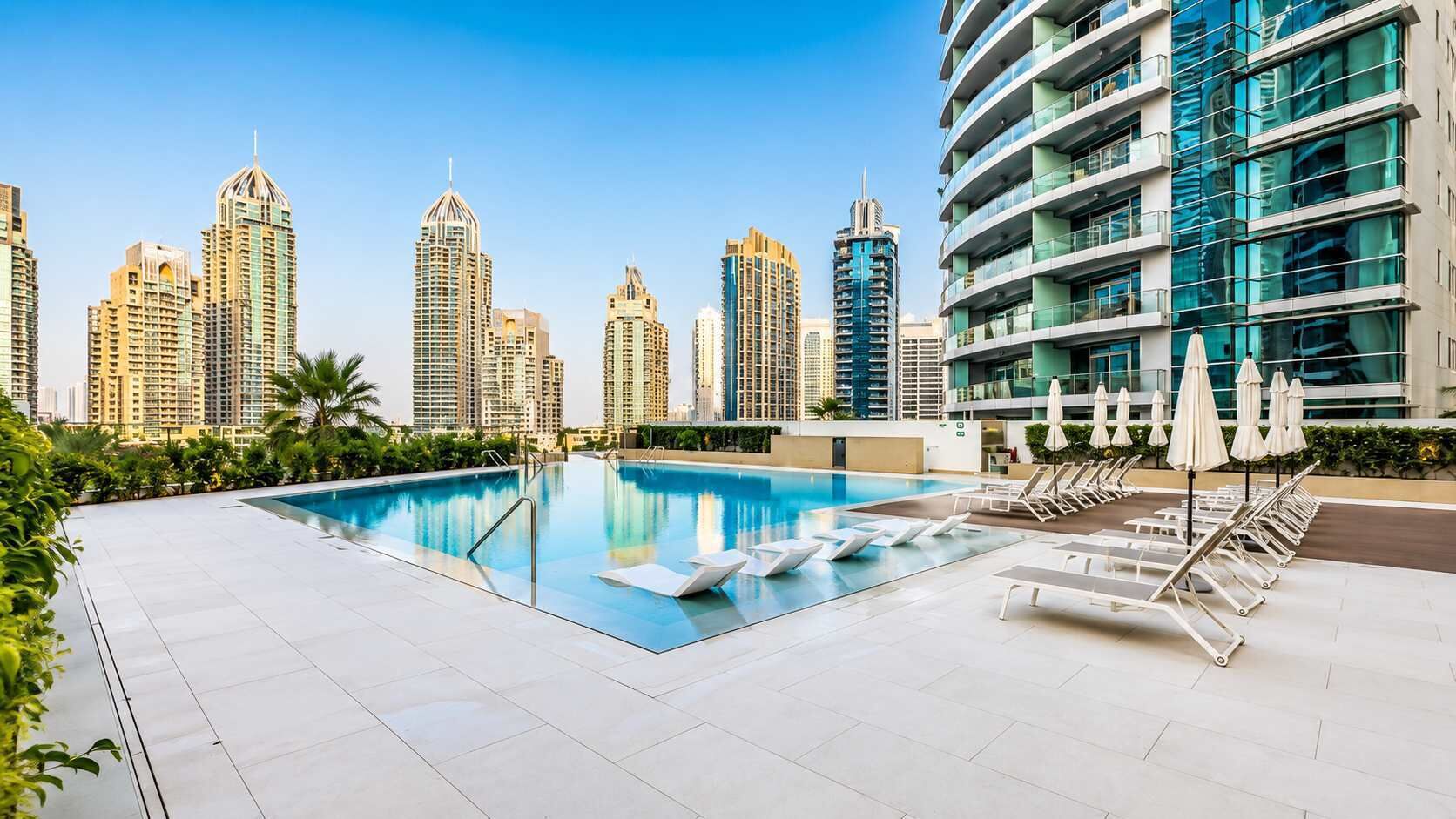 A rooftop swimming pool with lounge chairs and umbrellas, surrounded by high-rise buildings.