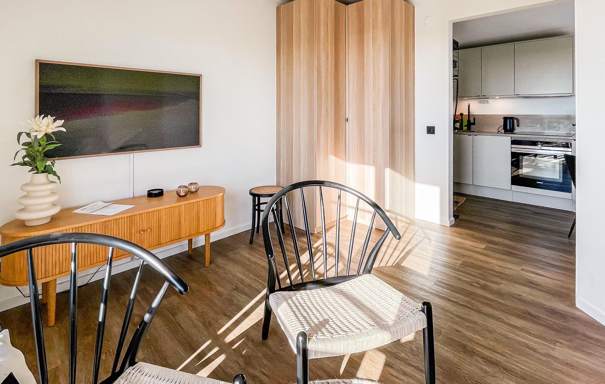 Ett modernt kök med vitvaror i rostfritt stål, en matplats med träbord och stolar samt en stor, abstrakt målning på väggen.